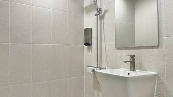 A modern bathroom with a freestanding sink, a handheld showerhead, and a mirror above the sink.
