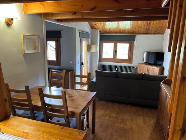 A cozy room with a wooden dining table, chairs, a sofa, and a television. - Cozy apartment in La Molina (La Molina)