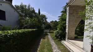 A pathway leading to a building with stone architecture, surrounded by greenery and a white wall. - Apartment Dory (Malinska-Dubasnica)