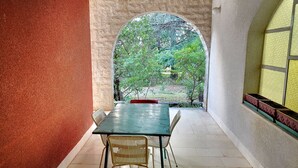A room with a table and chairs, a window with a view of greenery, and a textured wall. - Apartment Dory (Malinska-Dubasnica)
