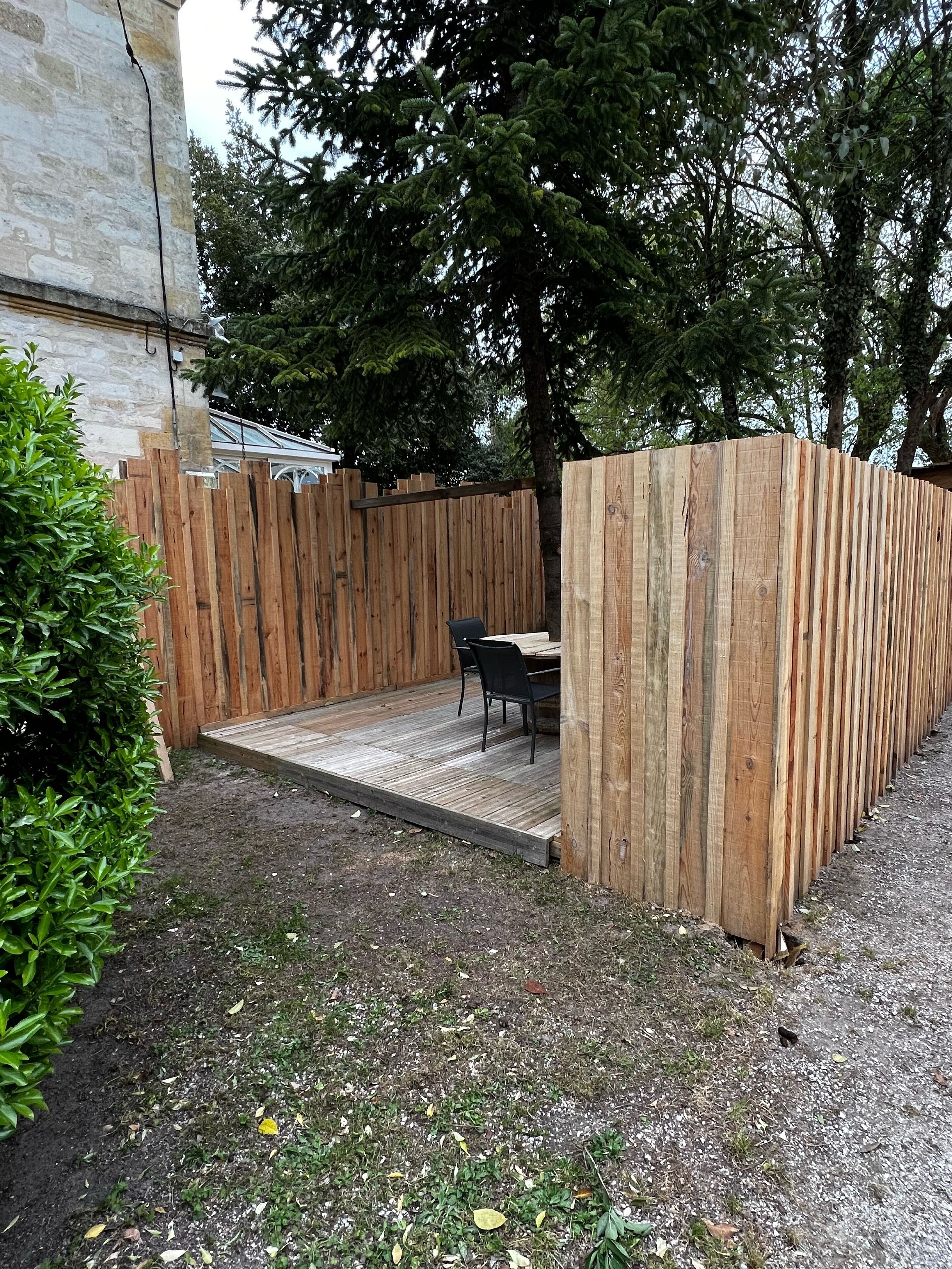 Een houten terras met een tafel en stoelen, omgeven door een houten hek en een kleine tuin.