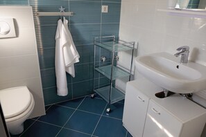 Un baño con un inodoro blanco, un estante de vidrio y un lavamanos blanco con un espejo encima.