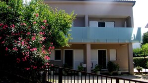 A two-story building with a balcony, a covered entrance, and a garden with pink flowers. - Apartment Dubravka (Malinska-Dubasnica)