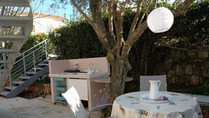 An outdoor patio with a table set for dining, a grill station, and a staircase leading to an upper level. - Apartment Dubravka (Malinska-Dubasnica)