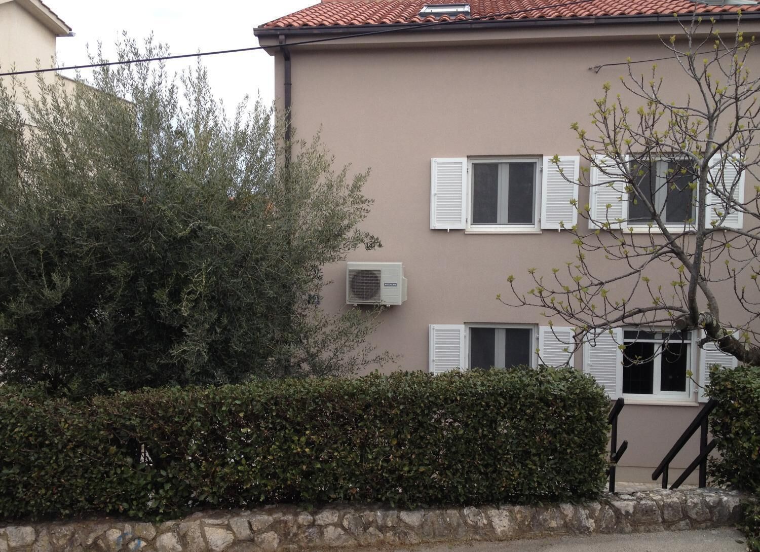 A building with a beige facade, white shutters, and an air conditioning unit.