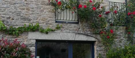 A stone building with a large glass door and a balcony with red flowers.