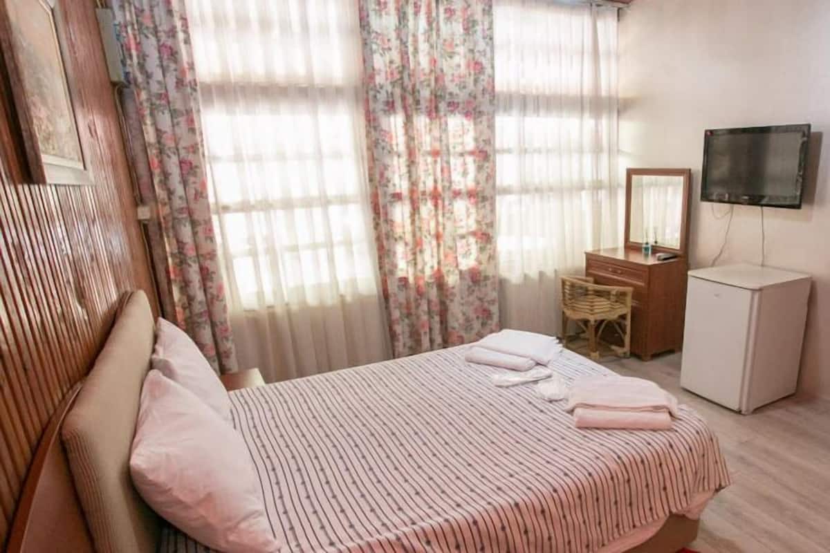 A hotel room with a bed, a desk with a mirror, a television, and a wardrobe.