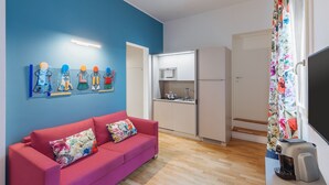 Una sala de estar moderna con un sofá rojo, una zona de cocina con armarios blancos y una cortina colorida.