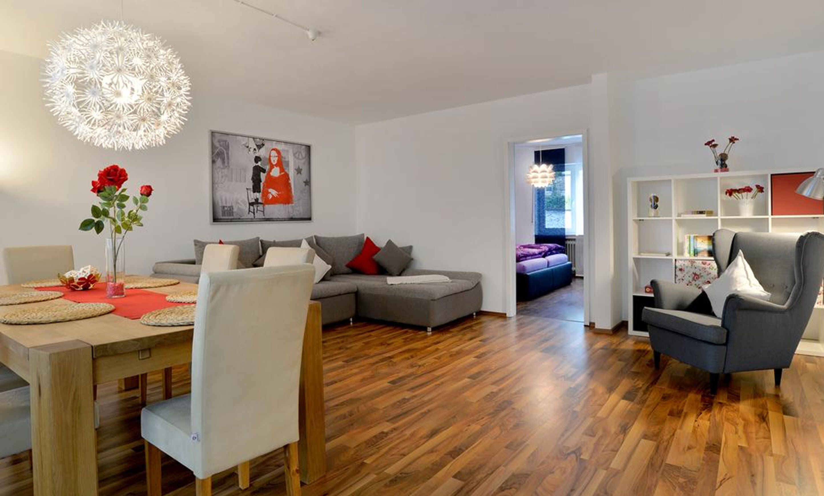 Una sala de estar moderna con un sofá gris, una mesa de comedor con sillas y una estantería.