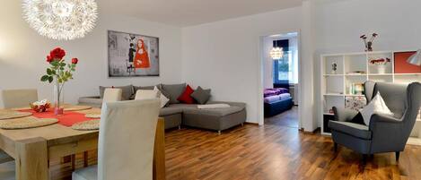 Una sala de estar moderna con un sofá gris, una mesa de comedor con sillas y una estantería.