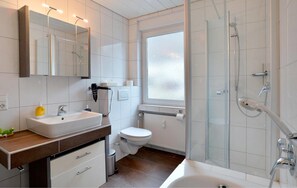 Un baño moderno con un espejo grande, un lavamanos, un inodoro y una zona de ducha.