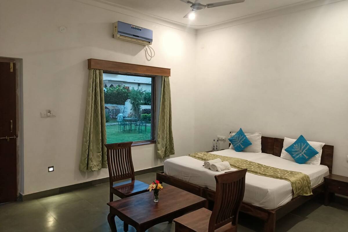 A hotel room with a bed, a desk, a chair, a window with curtains, an air conditioning unit, and a ceiling fan.