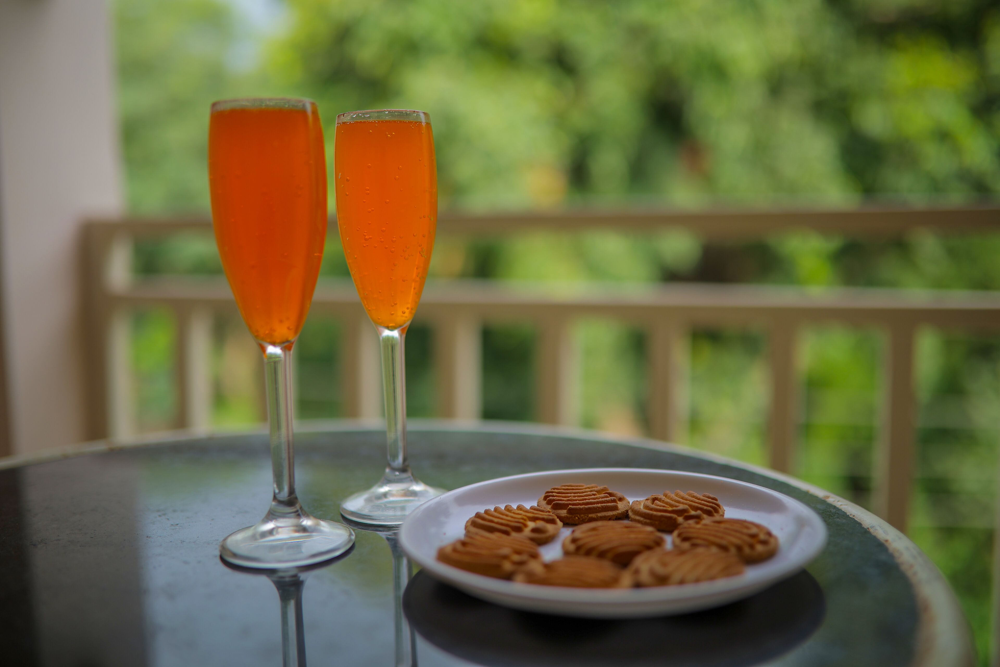 Two glasses of orange beverage on a table with a plate of cookies.