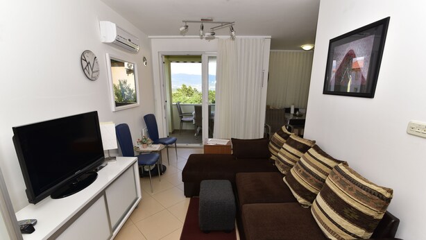 A living room with a flat-screen TV, a sofa, a coffee table, and a dining area with chairs. - Apartment Gloria (Dobrinj)
