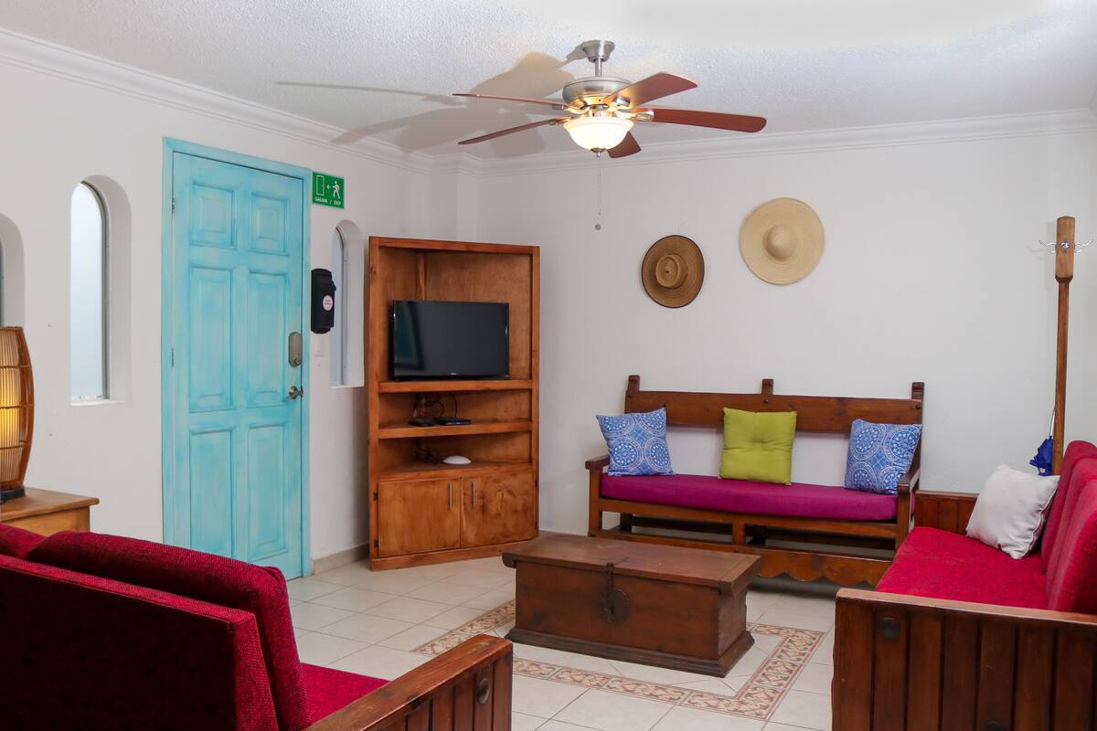 Una sala de estar con televisión, muebles de madera, ventilador de techo y una puerta azul.