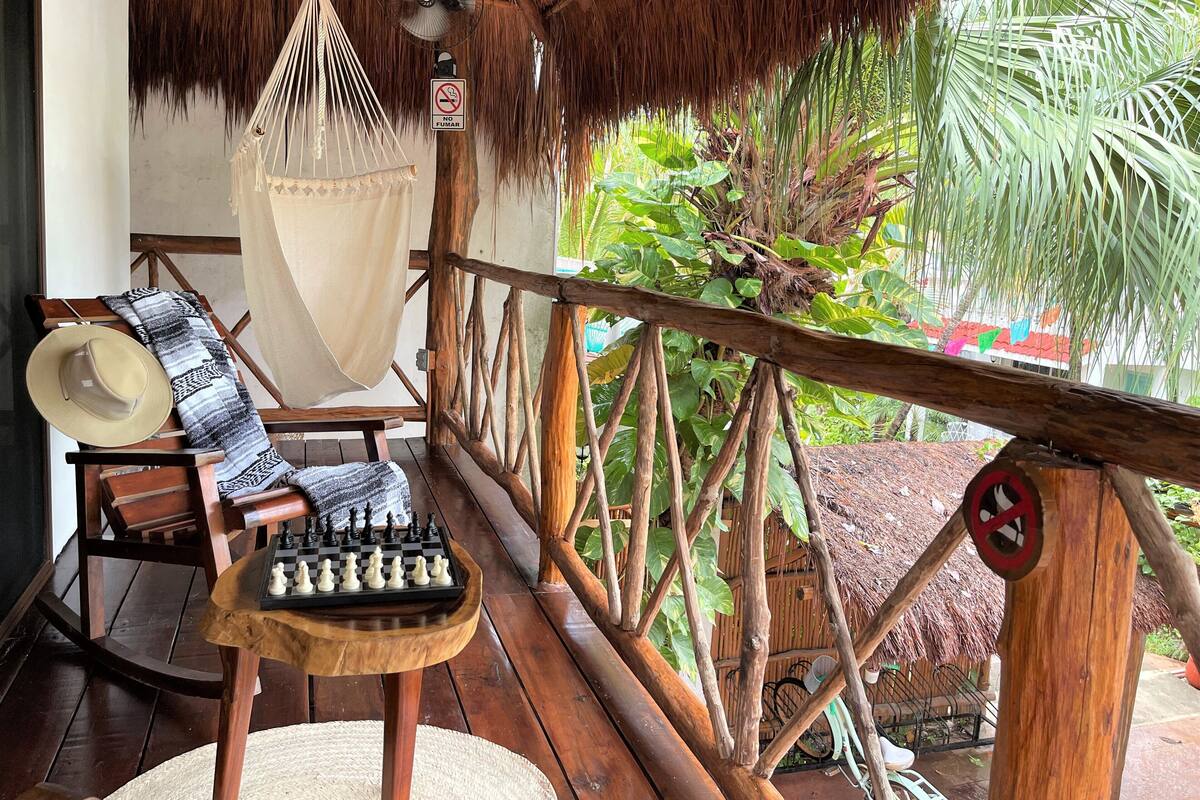 Una terraza de madera con un tablero de ajedrez, una hamaca y un techo de paja.