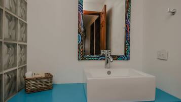 A bathroom with a white sink, a blue countertop, a decorative mirror, and a wicker basket with a tissue.