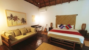 Een kamer met een bed, een bank, een gitaar en een schilderij van palmbomen.