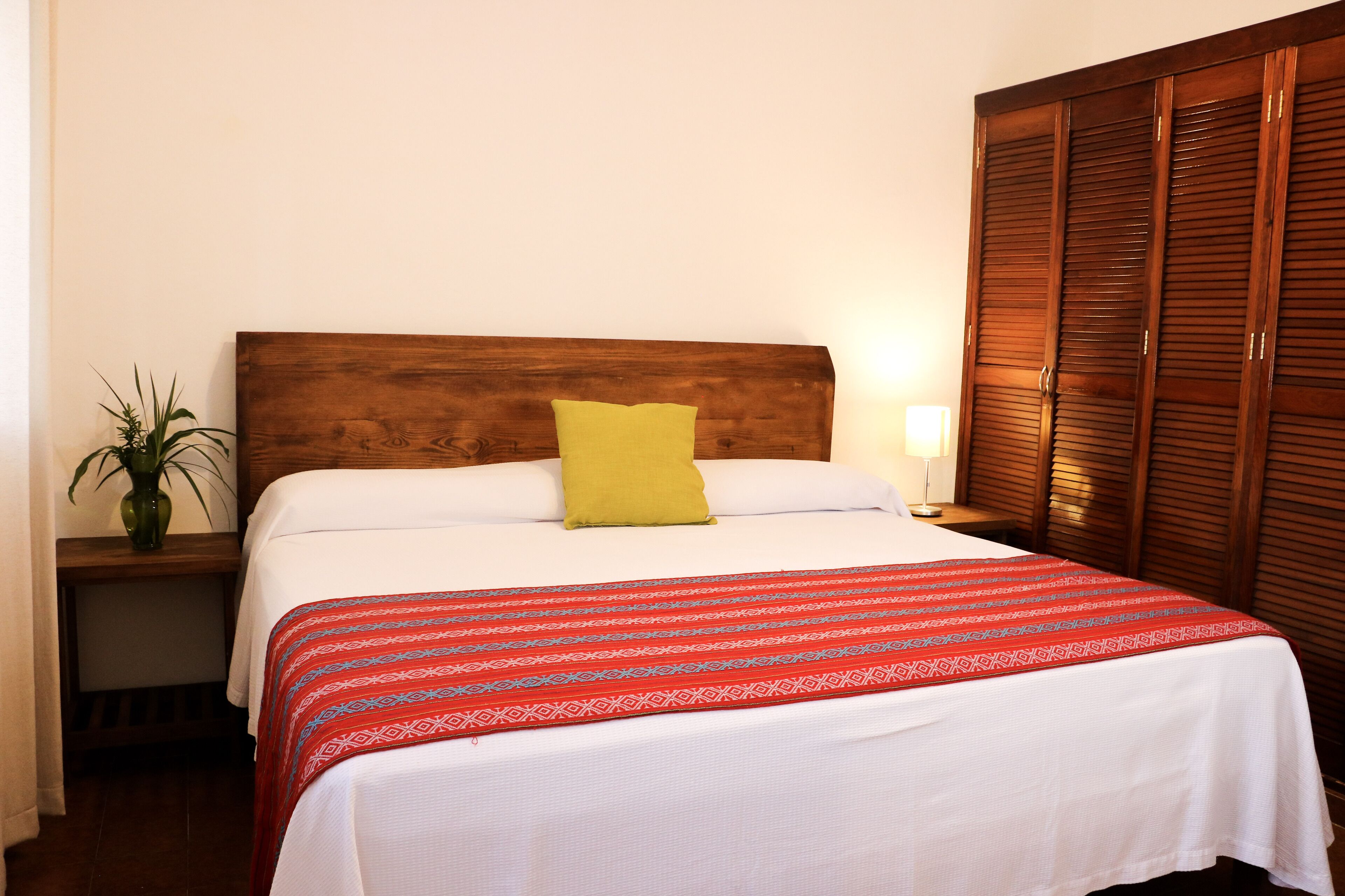 A neatly made bed with a patterned bedspread, a single pillow, and a bedside table with a lamp.