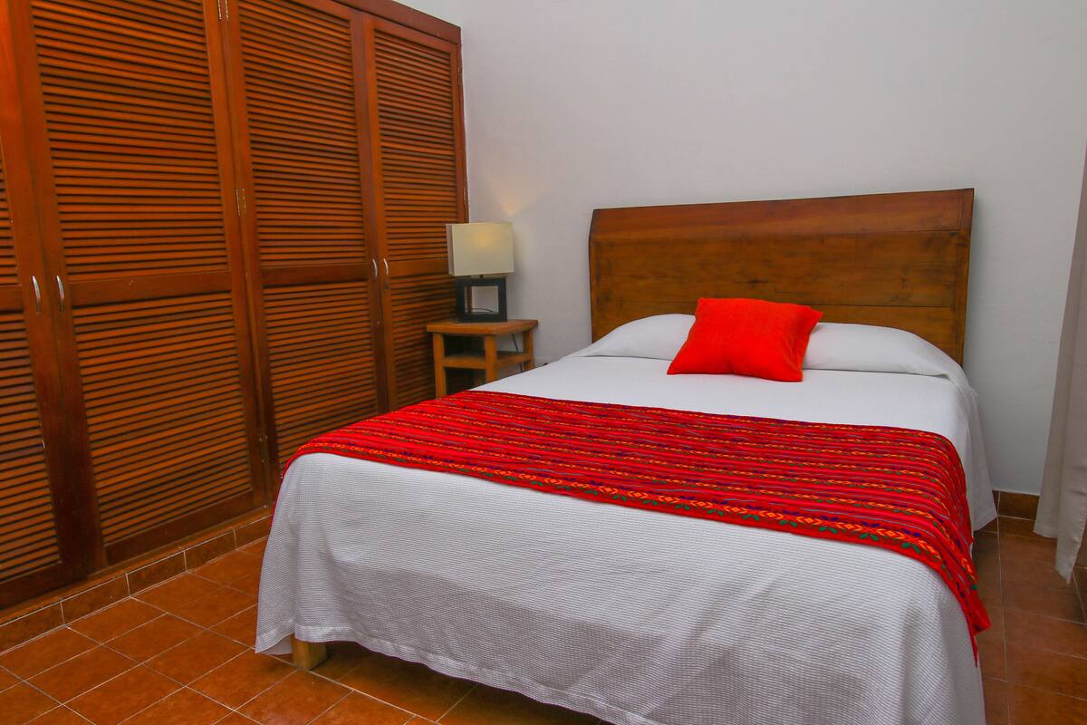 Una habitación de hotel con cama, mesita de noche, lámpara y armario.