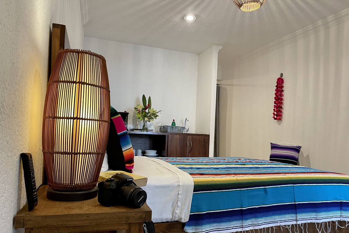 Un dormitorio con una cama, una mesita de noche con una cámara, una lámpara y vistas al baño.
