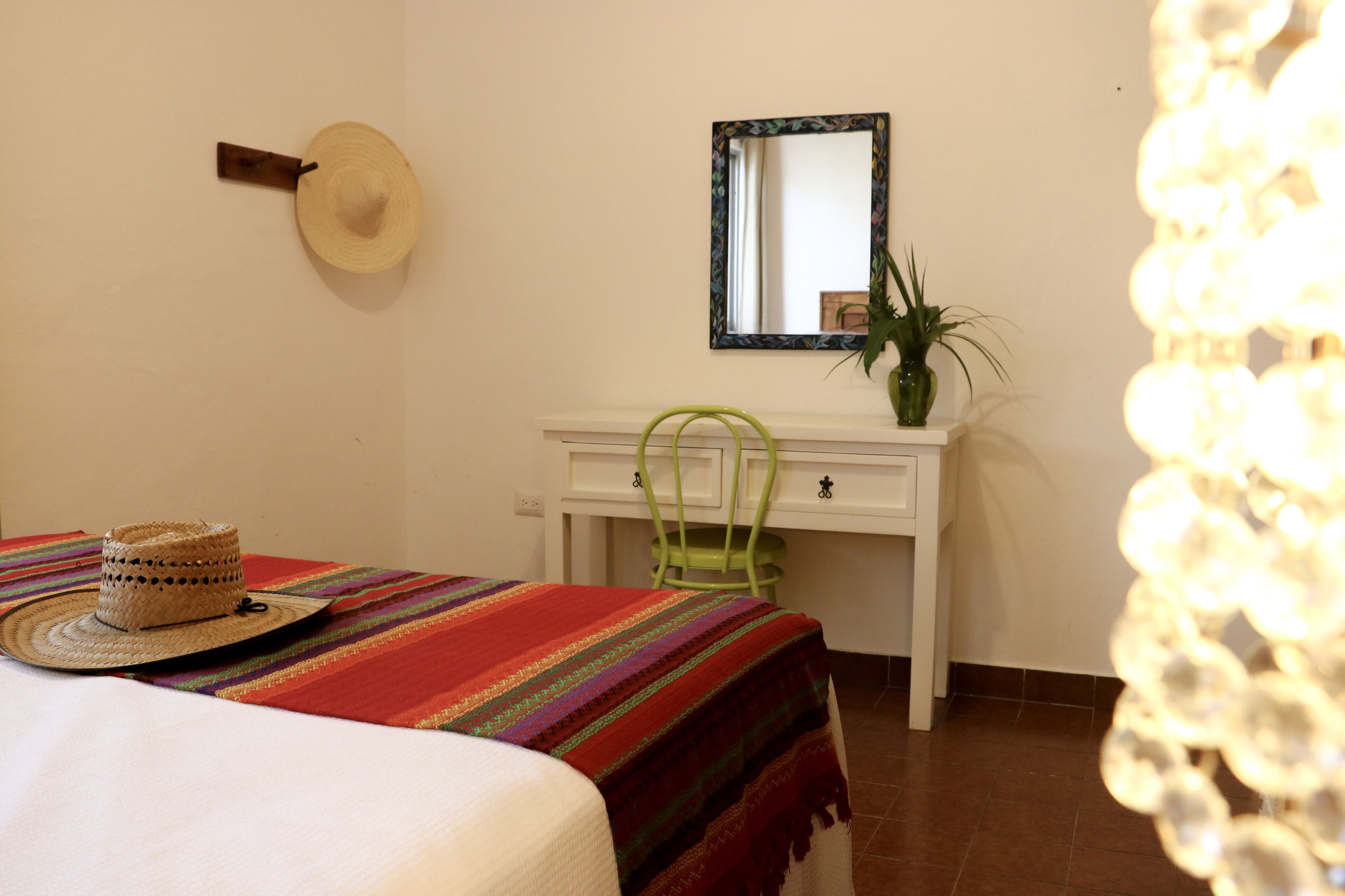 Una habitación con cama, escritorio, silla, sombrero y espejo.
