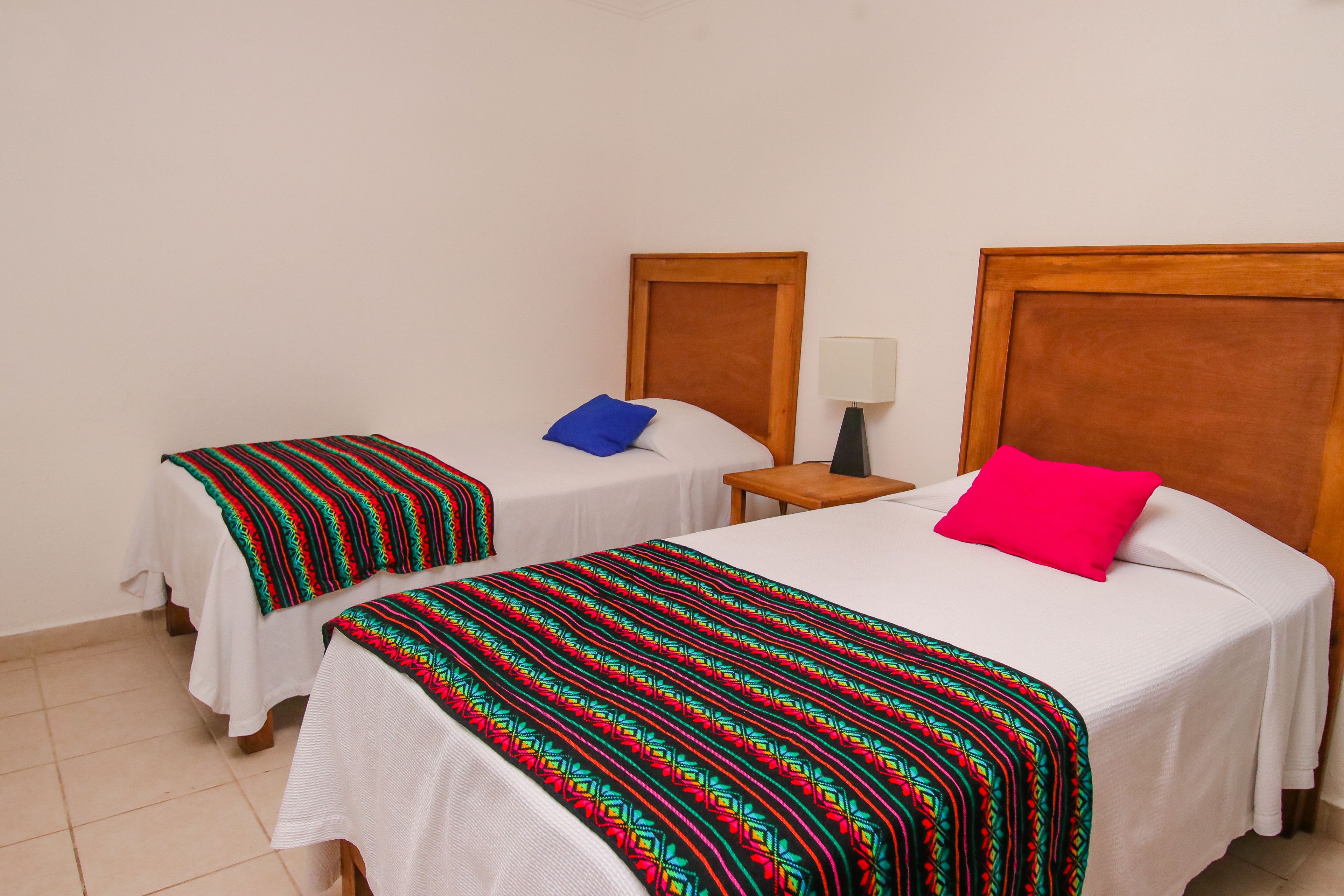 Two single beds with wooden headboards, white bedding, and colorful patterned blankets.