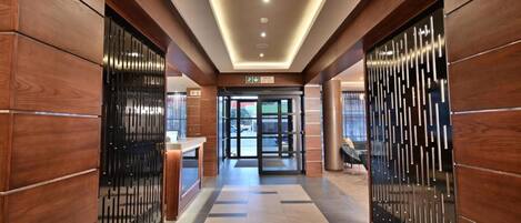 Un moderno vestíbulo de hotel con paneles de madera, un mostrador de recepción y un acceso por puerta de vidrio.