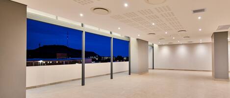 Amplio espacio interior, bien iluminado, con techos altos y diseño moderno, con ventanas grandes y vistas a un paisaje urbano al atardecer.