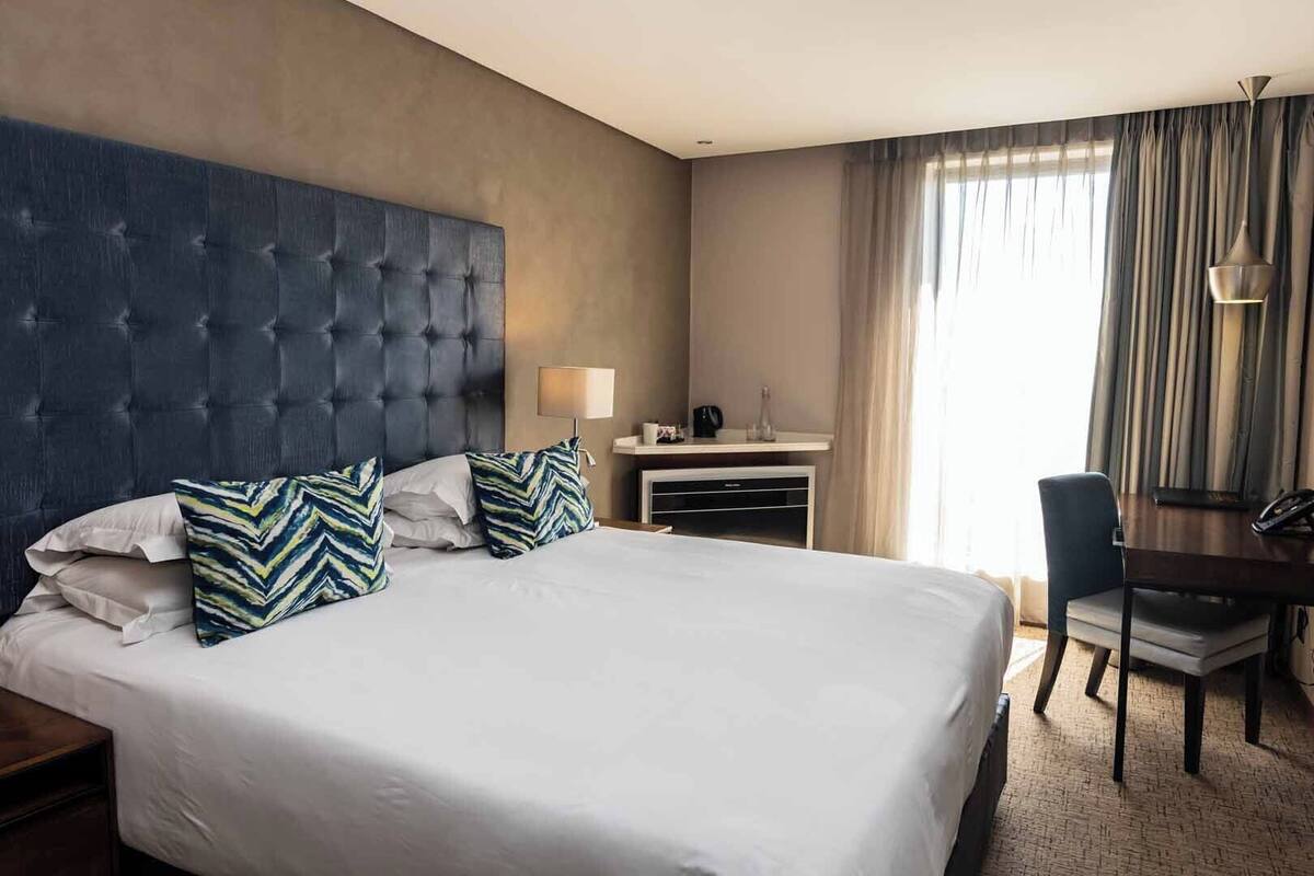 A hotel room with a large bed, a desk, a chair, and a lamp.