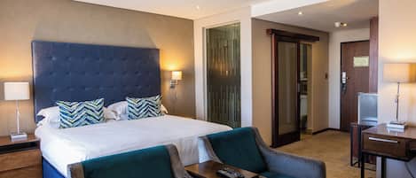 Una camera d'albergo con un letto grande, due poltrone, una scrivania e un televisore.