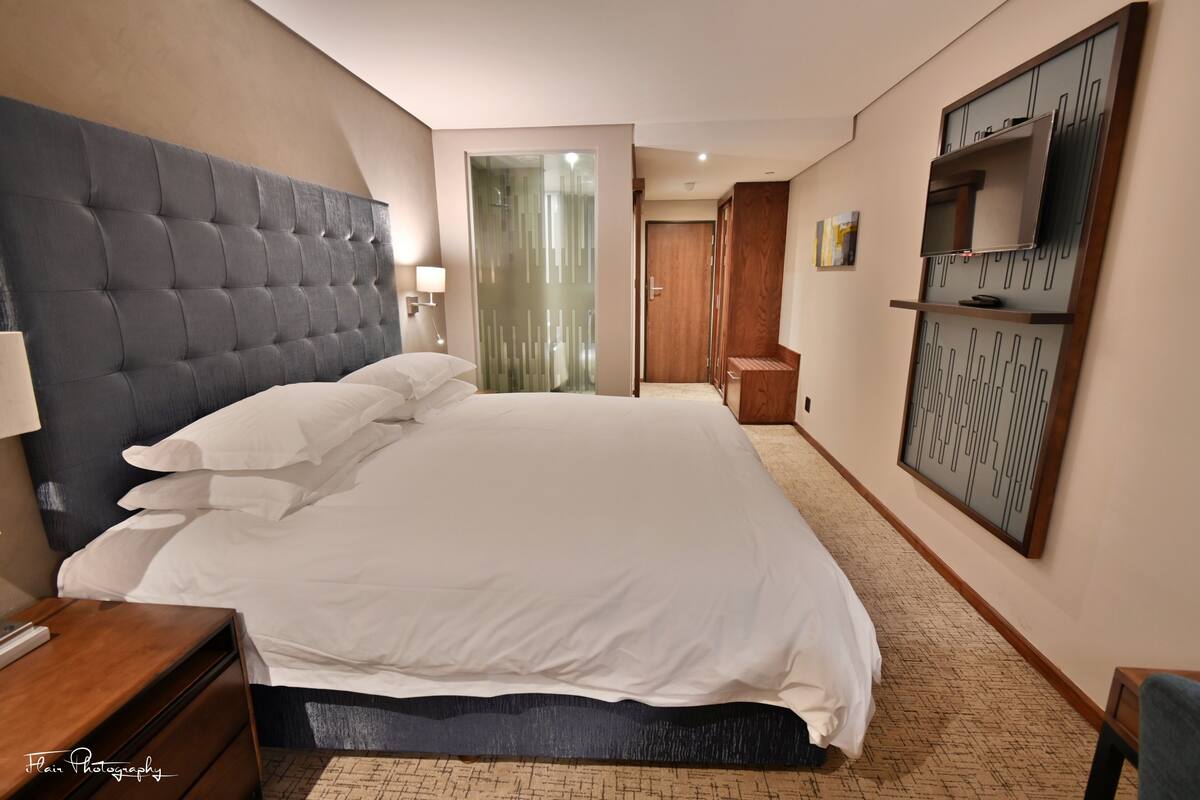 A hotel room with a large bed, a nightstand, a desk, a wardrobe, and a TV mounted on the wall.