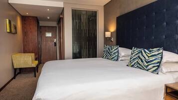 A hotel room with a large bed, a wooden chair, a glass door, and a dark headboard.