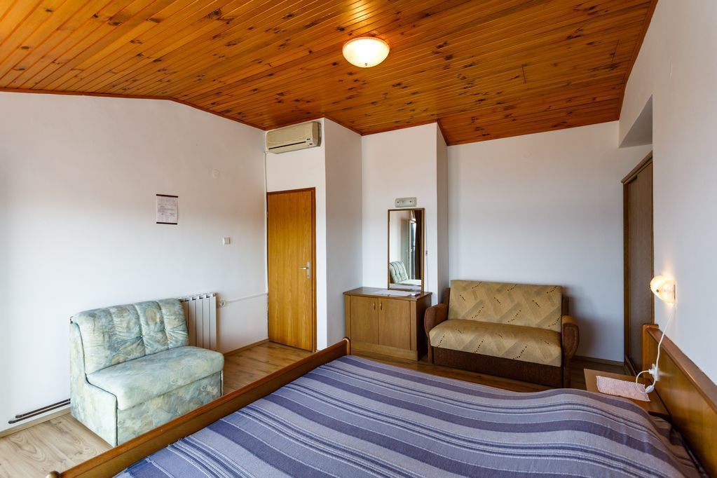 Une chambre avec un plafond en bois, un lit recouvert d’une couvre-lit à rayures, un canapé, une chaise et une petite table de chevet avec une lampe.