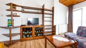 Ein Wohnzimmer mit Fernseher, Holzregalen, einer Vitrine und einem Sofa sowie einem Tisch.