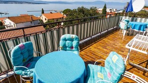 Ein Balkon mit rundem Tisch und zwei Stühlen, einer Satellitenschüssel und Blick auf einen See sowie Gebäude.