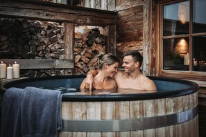 A wooden hot tub with a stone wall and candles in the background.