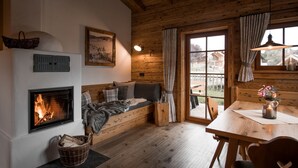 A cozy room with a fireplace, a sofa, a dining table, and a window with curtains. - Alpzitt - Chalets (Burgberg)