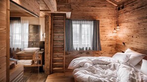 A wooden cabin bedroom with a bed, a window with curtains, a wooden ladder, and a bathroom with a sink and towels. - Alpzitt - Chalets (Burgberg)