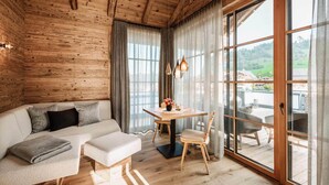 A cozy room with a wooden ceiling, a sofa, a table with chairs, and large windows offering a view of the outdoors. - Alpzitt - Chalets (Burgberg)