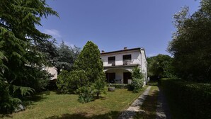 Une maison à deux étages dotée d’un balcon, entourée d’un jardin bien entretenu et d’un chemin pavé de pierres.