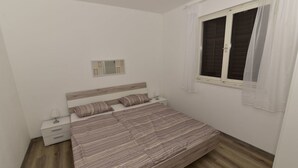 Une chambre à coucher comprenant un lit, une table de chevet, une fenêtre avec des rideaux et un petit miroir fixé au mur.