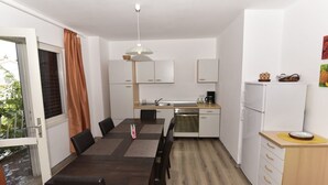 Une cuisine compacte avec un coin repas, des meubles blancs, une machine à café et un réfrigérateur.