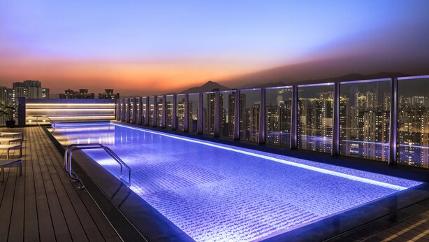 A rooftop pool with a city view at dusk. - Alva Hotel By Royal (Sha Tin)