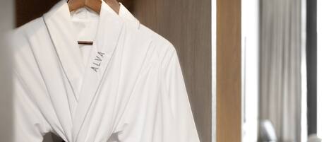 A white robe with "ALVA" embroidered on it hanging on a wooden hanger.