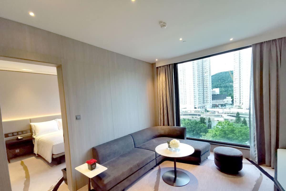 A modern hotel room with a large window, a sofa, a small table, and a bed.