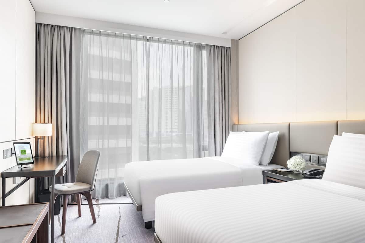 A hotel room with two beds, a desk, a chair, and a large window with curtains.