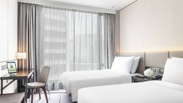 Ein Hotelzimmer mit zwei Betten, einem Schreibtisch, einem Stuhl und einem großen Fenster mit Vorhängen.