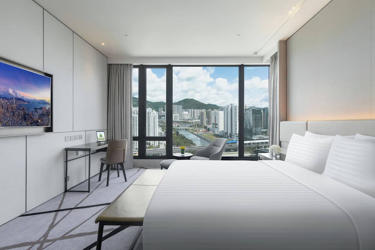 A modern hotel room with a large bed, a desk, a chair, and a TV.