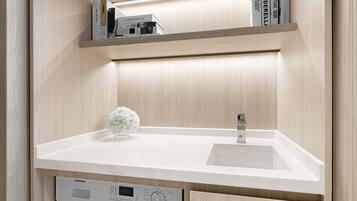 A compact laundry room with a washing machine, a sink, and a shelf with books.